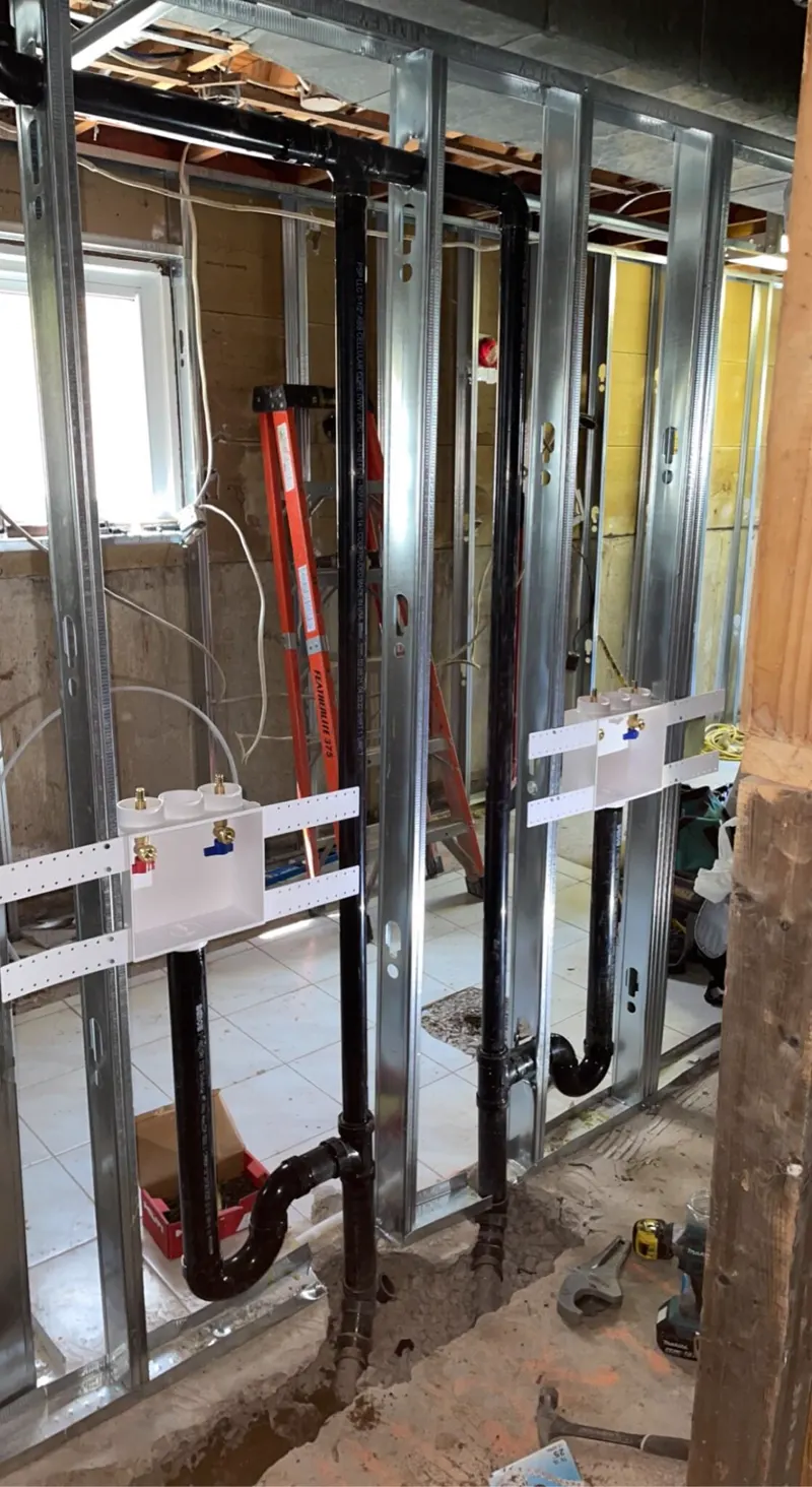 Basement plumbing rough-in with black ABS drain and vent lines and two laundry boxes in steel stud walls
