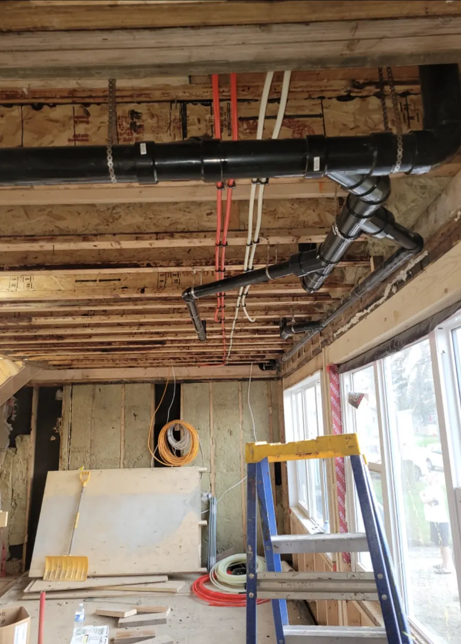 Black ABS drain line and red and white PEX water lines run through open ceiling joists during a renovation