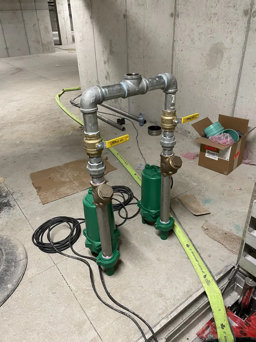 Two green submersible pumps with galvanized discharge piping and valves on a commercial job