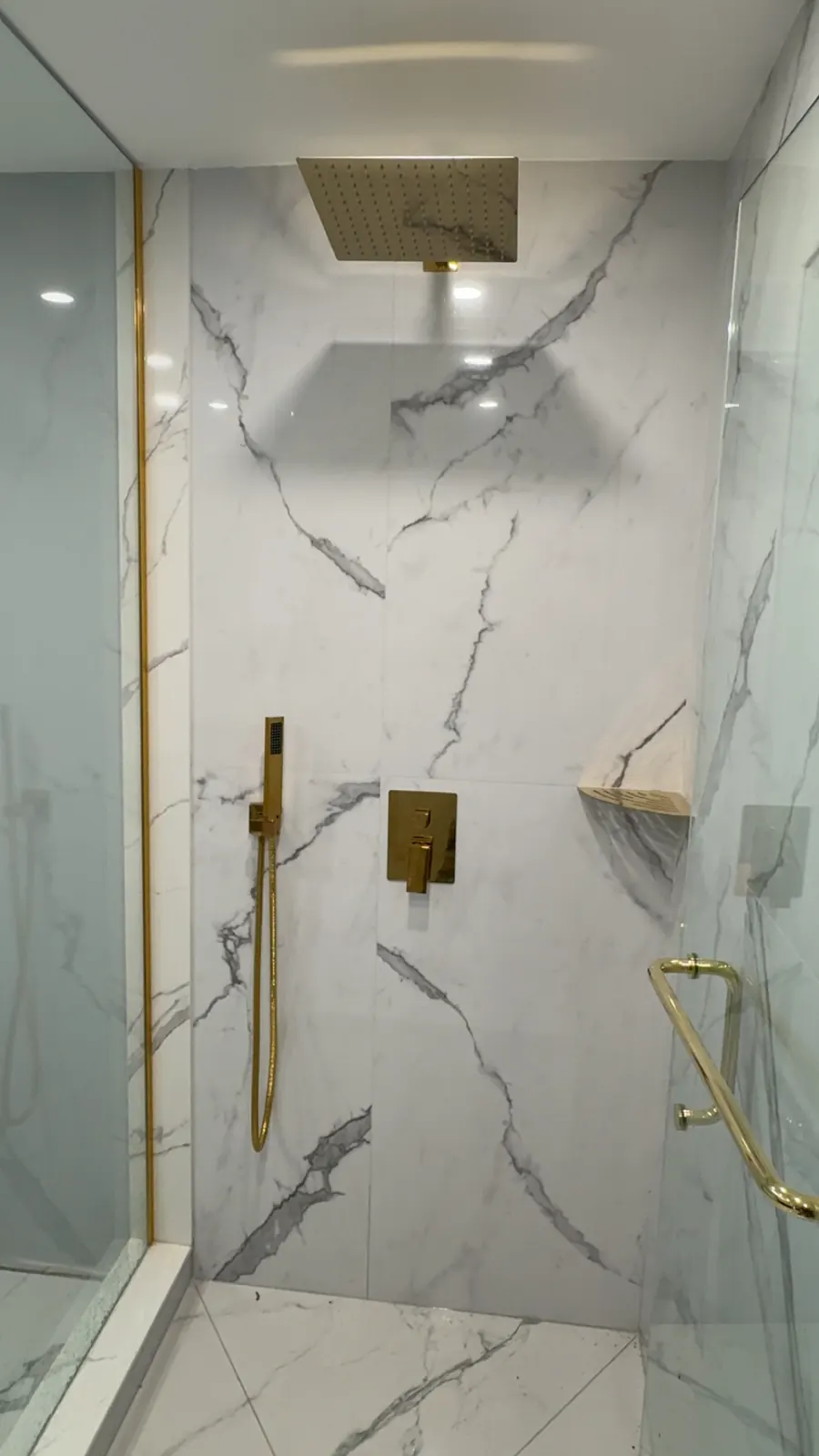 Glass shower enclosure with a ceiling rain head, brass slide bar hand shower and brass door handle