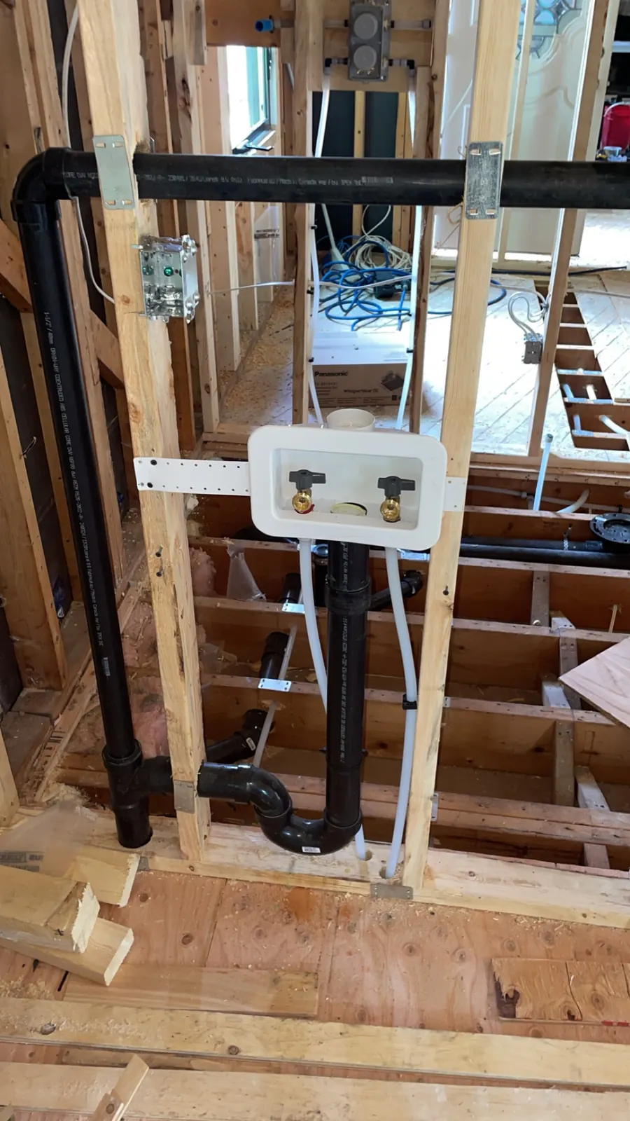 Laundry box with water valves and black ABS drain and vent piping roughed in through wood framing