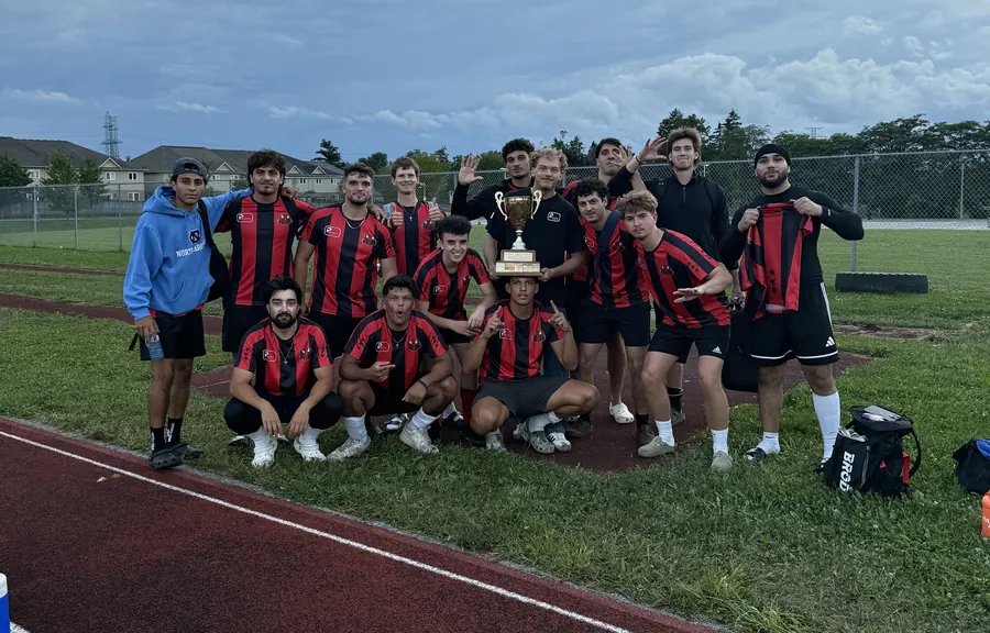 Local soccer team in red and black striped jerseys posing with a championship trophy on a field