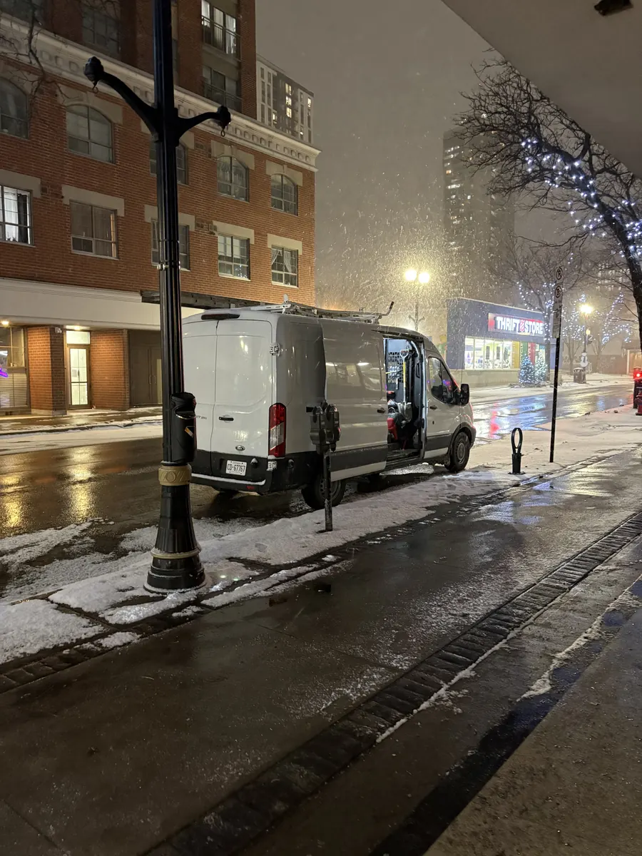 Panacci Plumbing's white work van parked on a snowy city street at night with its doors open