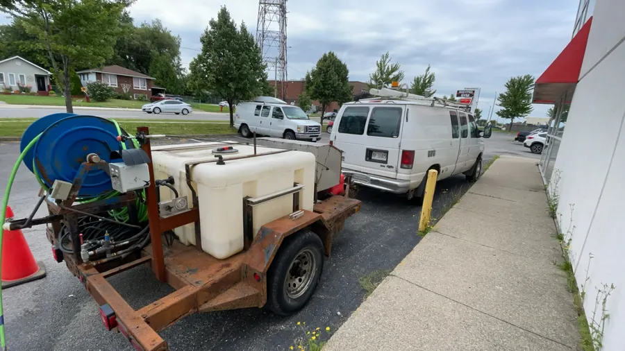 Sewer line cleaning trailer with hose reel and water tank parked at a commercial property